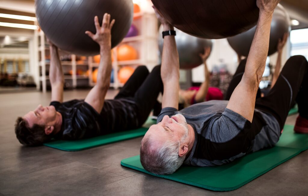 A group of cheerful seniors in gym doing exercise with fit balls.