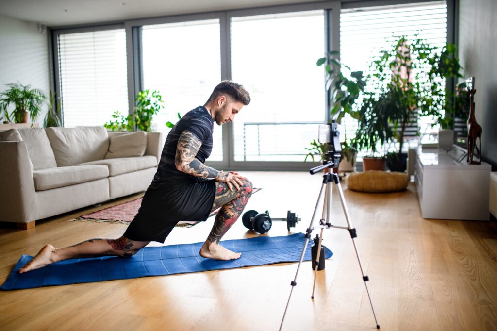 Man trainer doing online workout exercise indoors at home, using camera